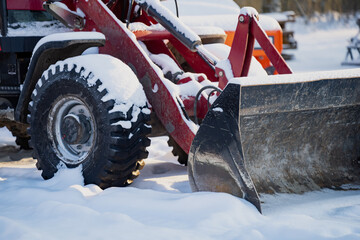 Front loader attachment of farm tractor with snowy tire and dirty steel bucket, close view of winter equipment used for snow removal and rural work