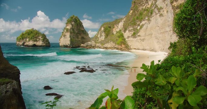 Turquoise ocean waves and sandy shore with high rock cliffs at Diamond Beach in Nusa Penida