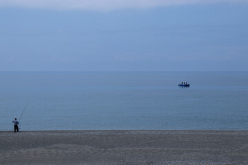 Pescatore sulla spiaggia e pescatori sulla barca