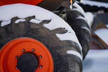 Orange rim wheel and wide rubber tire on loader or tractor, close up winter equipment detail with snow on tread blocks and blurred background