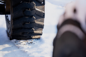 Heavy machinery wheel with thick tread pattern standing on snow, close up of industrial tire and ground texture with shallow depth of field and soft light