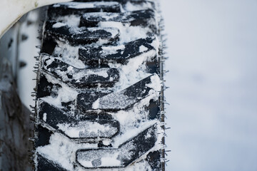 Close up of studded winter tire tread covered with packed snow, rugged rubber pattern on construction equipment wheel beside white body panel in cold daylight