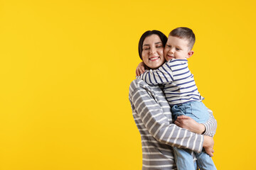 Fototapeta premium Happy mother hugging her son on yellow background, space for text