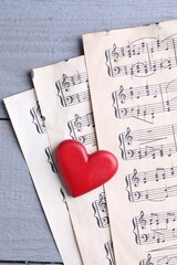 Heart figure and paper sheets with music notes on gray wooden table, top view