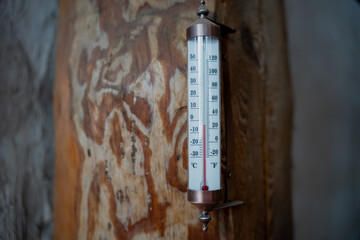 Vintage wall thermometer with Celsius and Fahrenheit scale mounted on rustic wood beam, close up of indoor temperature gauge with shallow depth of field