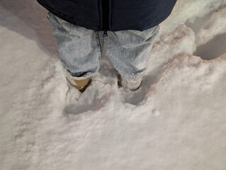 Person standing in deep fresh snow, view of winter boots and legs. Cold outdoor lifestyle scene and seasonal weather concept.
