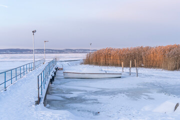Frozen pier and boat with reeds on the icy lake in winter, in Lake Balaton, Hungary