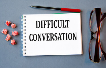 DIFFICULT CONVERSATION - words in notebook on gray background with glasses and pen