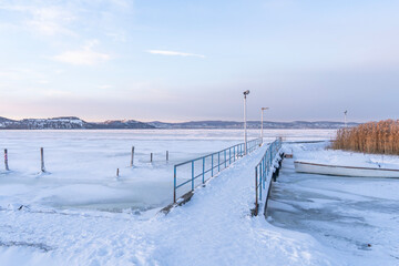 Frozen pier and boat with reeds on the icy lake in winter, in Lake Balaton, Hungary