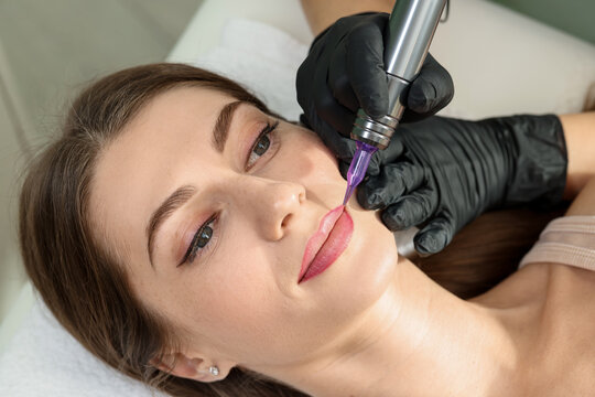 Beautician making permanent lip makeup to young woman indoors, closeup