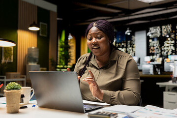 African american person joining a web video conference on laptop, engaged in a digital discussion late at night. Woman interacting with coworkers team, adaptability in networking session.