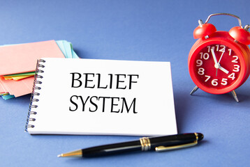 BELIEF SYSTEM - words in notebook on blue background with watch and pen
