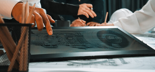 A diverse team collaborates in a modern office, analyzing a detailed blueprint on a tablet. The focus is on teamwork and creative ideas in a professional environment. SACTR