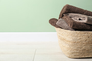 Obraz premium Laundry basket with towels on floor near green wall indoors, closeup. Space for text