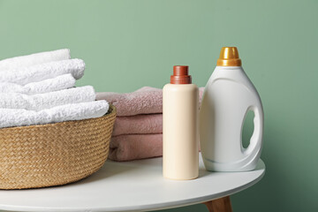 Laundry basket with towels and bottles of detergent on table near green wall indoors