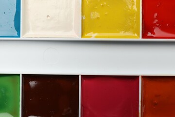 Palette with watercolor paints as background, top view