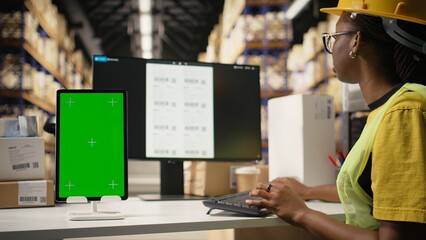 Black employee with hard hat manages tracking info next to mockup display, overseeing shipment...