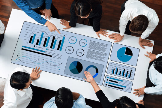 A diverse group of business professionals gathered around a table, actively analyzing graphs and charts to discuss strategies, performance metrics, and project outcomes. Gantry