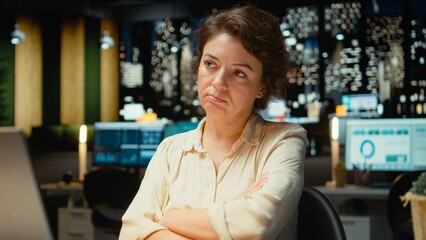 Female employee at night sighing and feeling tensed at work, being overwhelmed and pushing limits despite clear signs of weariness. Workplace challenges and discouragement bring discomfort. Camera A.