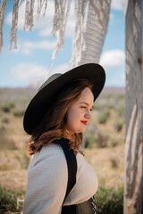 Woman smiles in a field wearing a hat while enjoying a sunny day outdoors among plants and greenery