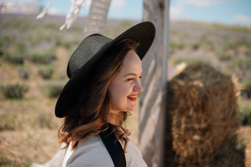 Woman smiles in a field wearing a hat while enjoying a sunny day outdoors among plants and greenery