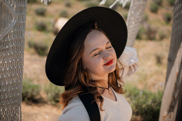 Woman smiles in a field wearing a hat while enjoying a sunny day outdoors among plants and greenery