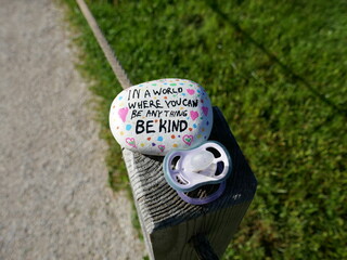 Fence post with baby pacifier and be kind kindness rock