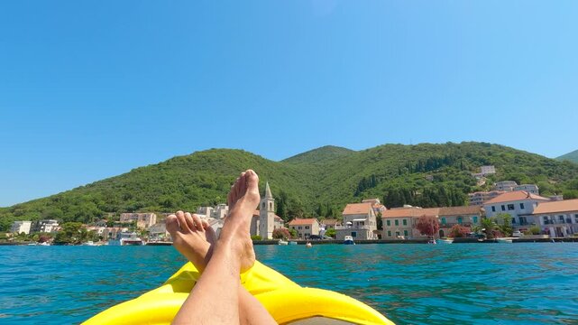 Tourist kayaking in the bay of kotor with feet up enjoying picturesque town. Legs and bare feet of a tourist relaxing on an inflatable yellow kayak, enjoying the breathtaking view