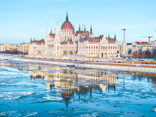 Fototapeta premium The Parliament of Hungary in Icy Winter time and it's mirrored picture on the freezing Danube, Budapest Hungary
