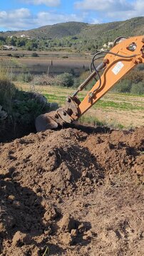 Mini excavator digging a trench and removing soil in the field