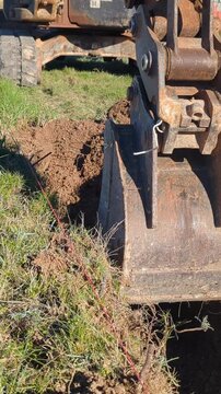 Close-up of the arm and bucket of a mini excavator digging a trench for a foundation