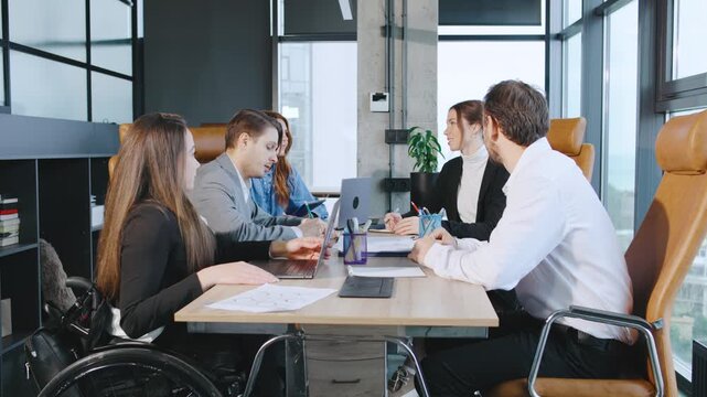 Team members brainstorm in the carpet area and pass around papers with charts and valuable information, focusing on inclusivity and diversity while ensuring wheelchair accessibility when discussing