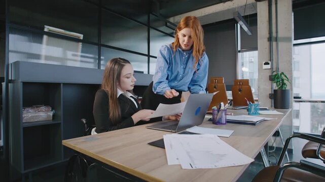 Two professionals discuss work at a shared desk in a modern office. The space supports diverse teamwork and includes accessibility features.