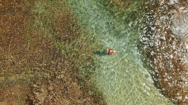 Single swimmer woman floating in clear tidal pool among reef rock on Caribbean shore
