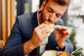 Businessman in a suit eating a delicious sandwich, hungry male professional having a quick lunch break during work.