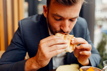 Businessman in a suit eating a delicious sandwich, hungry male professional having a quick lunch break during work.
