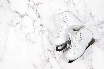 A pair of white figure skates shoes with sharp steel blades, laid flat on a white marble surface, ideal for winter sports themes, fitness content, or seasonal holiday promotions.