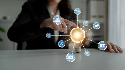 A professional in a modern workspace interacts with a glowing light bulb surrounded by digital icons, representing innovation and technology in business. Crux