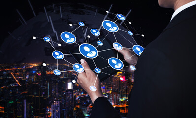 A businessman interacts with a digital interface featuring social icons, symbolizing global connections and innovation against a vibrant city backdrop at night. Tessel