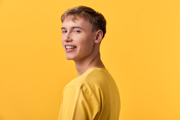 Fototapeta premium Smiling male model in a yellow shirt poses against a bright yellow studio backdrop, radiating warmth, positivity, and casual confidence for lifestyle or fashion use