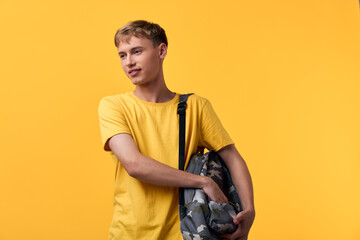 Youth man wearing a yellow t shirt with a camouflage backpack slung over one shoulder, posed...