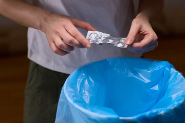 Hands discarding expired pills into bin, closeup of blister pack over blue plastic liner, tabletop...
