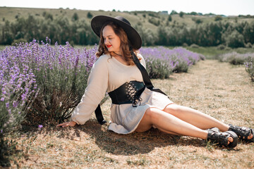 Woman sits in lavender field wearing a black hat and enjoying the sunlight during a warm day in summer