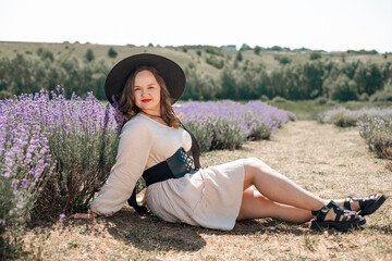 Woman sits in lavender field wearing a black hat and enjoying the sunlight during a warm day in summer