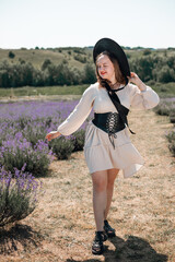 Woman sits in lavender field wearing a black hat and enjoying the sunlight during a warm day in summer