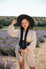 Woman sits in lavender field wearing a black hat and enjoying the sunlight during a warm day in summer
