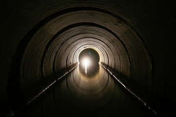 Inside dark round underground urban flooded sewer tunnel with water reflection