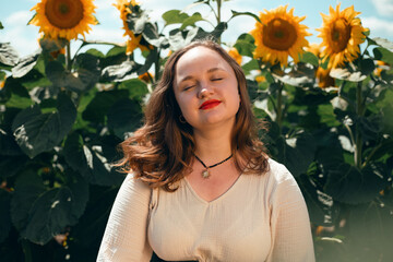 Sunflowers bloom in a field while a woman smiles in front of them on a sunny day during the summer season in a rural area