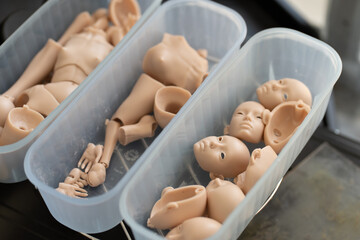 Closeup of silicone doll parts in containers, including various body and face pieces. Parts are awaiting assembly in the doll-making process