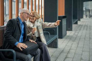 Senior couple taking selfie enjoying coffee on urban bench